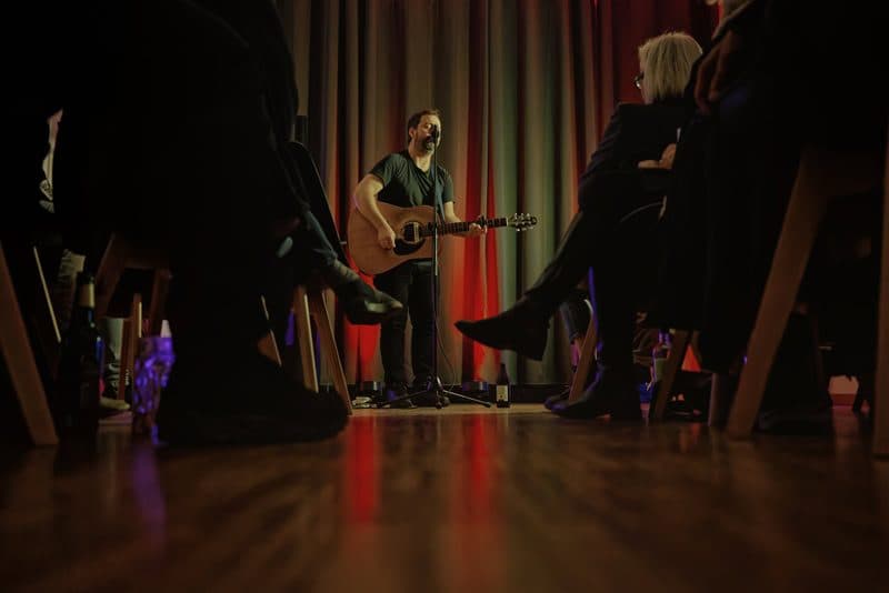 Singer-Songwriter mit Gitarre vor sitzendem Publikum in der Bar & Gallery