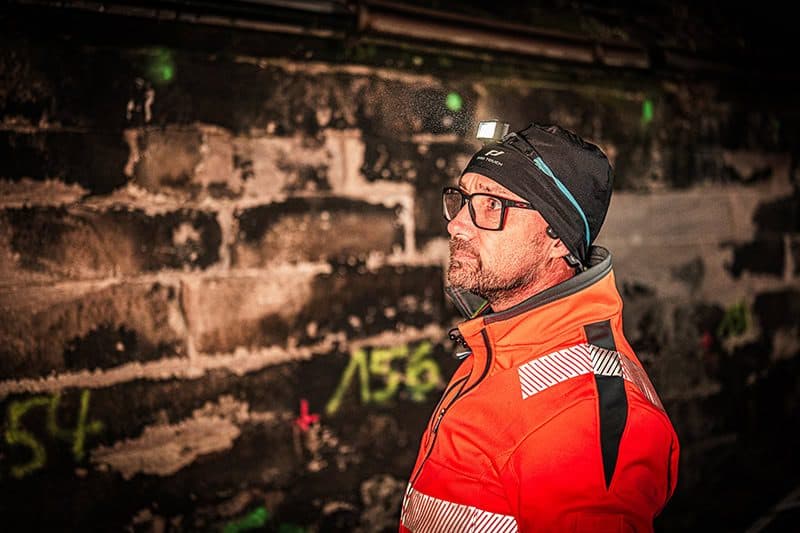 Inspektion im Kanal: Ingenieur mit Stirnlampe vor markiertem Mauerwerk